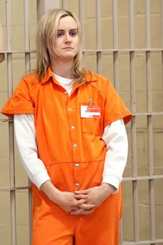 a woman in an orange jumpsuit standing next to a jail cell