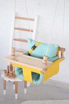 a yellow swing chair with blue and green pillows hanging from it's sides, in front of a white wall