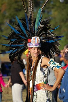 a native american woman wearing a headdress at an outdoor event with other people in the background