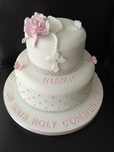 a three tiered cake with pink and white flowers on it's side, sitting on a black surface