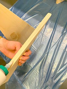 a person holding a piece of wood in front of a blue tarp covered table