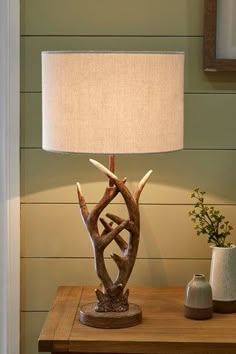 a lamp on a wooden table next to a vase with flowers in it and a deer antler