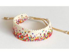 two bracelets with multicolored beads are on a white surface and one has a string