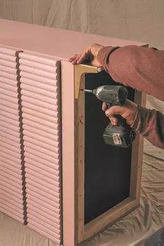 a person using a power drill to attach the shutters on a pink painted cabinet