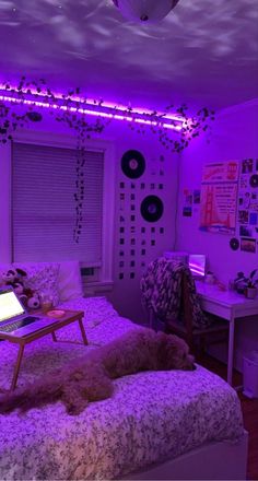 a bed with purple lights in a bedroom next to a desk and laptop on top of it