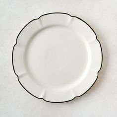 an empty white plate with black trim on the rim and bottom, sitting on a plain surface