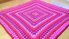 a pink and purple crocheted rug on the floor with wood floors in the background