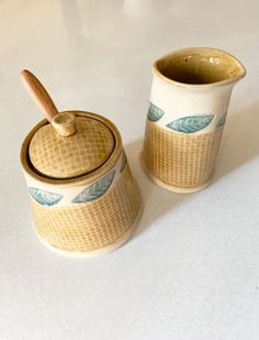 two ceramic containers with wooden spoons sitting on a white counter top next to each other