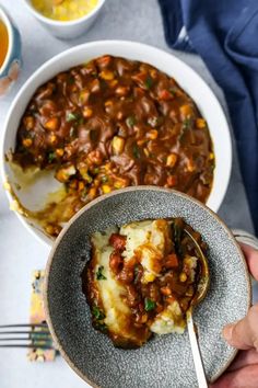 a person holding a spoon in a bowl filled with baked beans and mashed potatoes