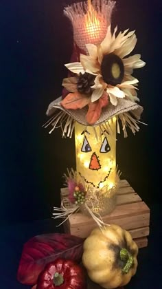 an arrangement of pumpkins and flowers in a vase with lights on it, sitting next to other decorations