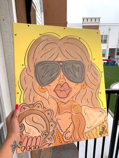 a woman holding up a drawing of a lady with sunglasses