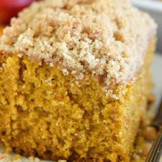 a close up of a piece of cake on a plate with a fork and an apple in the background