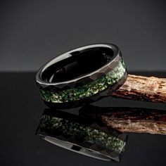 two wedding bands with green and black stones on them, sitting next to each other