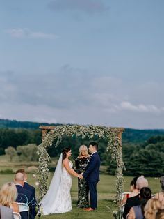 a bride and groom standing at the end of their wedding ceremony under an arch decorated with greenery