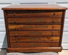 an old wooden chest of drawers with writing on the front and sides, sitting in front of a garage door