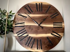 a large wooden clock with roman numerals on the face next to a potted plant