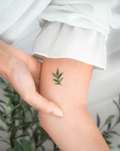 a woman's arm with a small green leaf tattoo on it