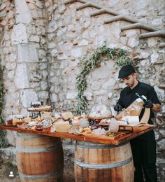 a man standing next to two wooden barrels with food on them and wine glasses in front of him