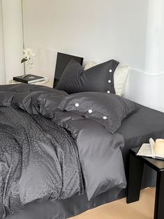 a bed with grey sheets and pillows in a white room next to a black end table