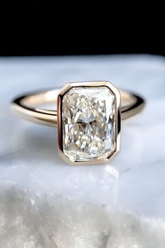 an engagement ring with a square cut diamond in the center on top of a marble slab