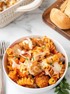 a white bowl filled with pasta and meatballs on top of a table next to bread