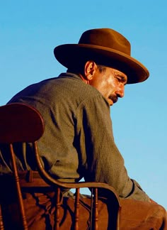 a man sitting in a chair with a hat on his head and looking down at the ground