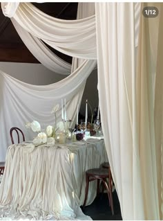 the table is covered with white draping and decorated with flowers in vases