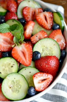 a bowl filled with cucumbers, strawberries and blueberries on top of a table