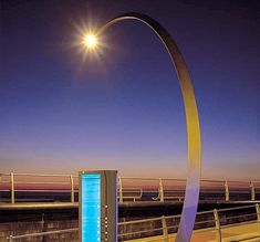 a street light next to a large metal sculpture in the middle of a road at night