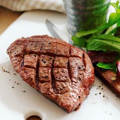 a piece of meat sitting on top of a white plate next to a green salad