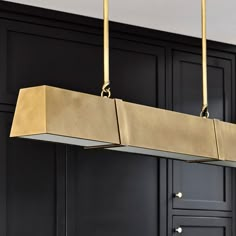 a large rectangular light fixture hanging from the ceiling in a black and gold colored kitchen