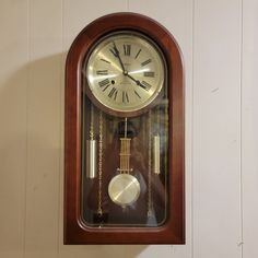 a wooden clock mounted to the side of a wall with chains hanging from it's sides