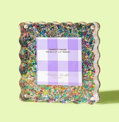 a purple and white photo frame with colorful sprinkles on the bottom, in front of a green background