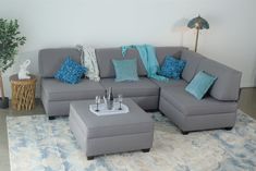 a gray sectional couch with blue pillows on it in a living room area next to a lamp