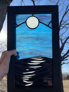 a hand holding up a stained glass window in front of a tree with blue sky and clouds