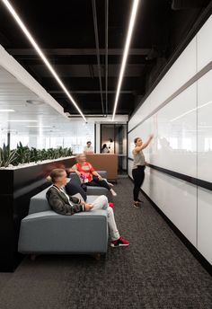 three people sitting on couches in an office with white walls and black flooring