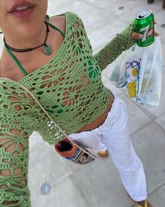 a woman wearing white pants and a green crochet top holding a can of soda