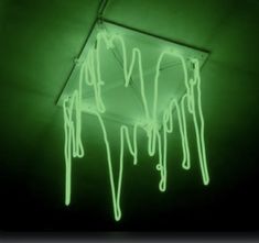 a neon green light hanging from the ceiling in a dark room with dripping paint on it