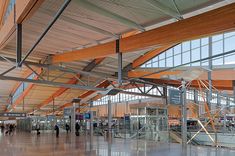 people are walking through an airport terminal with glass walls and wood beams on the ceiling