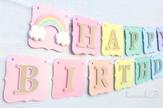 happy birthday banner with rainbows and clouds on the wall in pastel colors, hanging from hooks