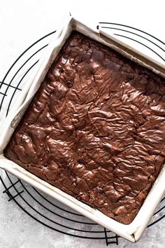 a square chocolate cake sitting on top of a wire rack in front of a white wall