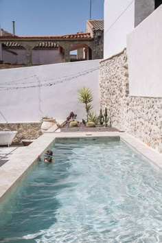 a person swimming in a small pool next to a building with a cactus on it