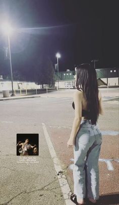 a woman standing in the middle of a parking lot at night with her back to the camera