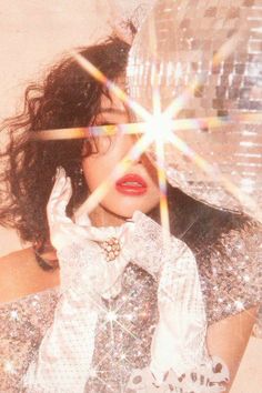 a woman with long hair and red lipstick holding her hands up to her face in front of a disco ball