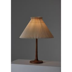 a lamp that is sitting on top of a white tablecloth with a wooden base and pleated lampshade