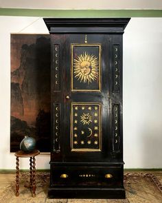 an ornate black cabinet with sun and moon designs on it's doors, in front of a painting