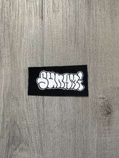 a black and white sticker on a wooden surface with the word's logo