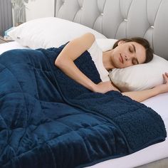 a woman laying in bed with a blue blanket and pillows on her back, she is sleeping