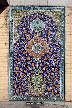 an ornate blue and orange rug hanging on the side of a building with a brick wall behind it