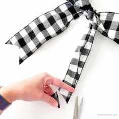 a person is cutting fabric with scissors on a white surface and tied to a black and white checkered ribbon